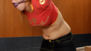 Barefoot Sharon in red top and black shorts, tied in the strappado kneeling on the floor with her hair tied to her wrist.webp