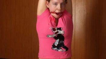 Barefoot ring-gagged Sharon in pink t-shirt and black shorts, frogtied with violet hemp rope, is being pulled up to stan.webp