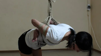 Ballgagged barefoot Ola in white t-shirt and black shorts, tied kneeling on the hard floor, is trying to handle her unco.webp