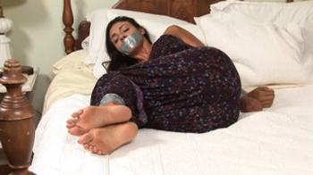 Barefoot brunette Tomi Taylor struggled on her bed tape-bound and tape-gagged after she was surprised by an intruder!.webp