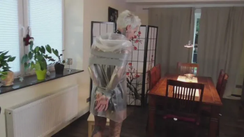 Miss Francine wird in einem knappen Lackoutfit und einem transparenten Regenmantel gefesselt und mit Tape geknebelt.webp